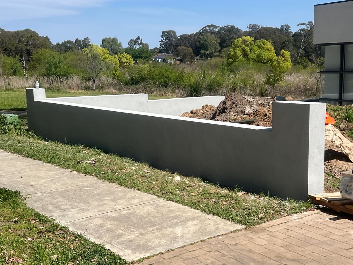 Charcoal rendered retaining wall with a contrasting white capping beside a Sydney footpath