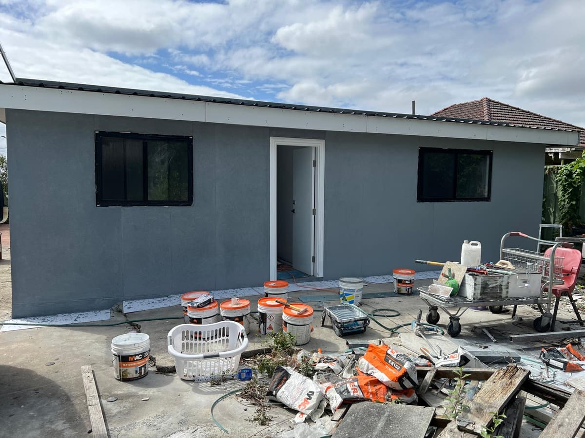 Charcoal grey texture coated granny flat exterior in Sydney with render buckets and tools on the slab
