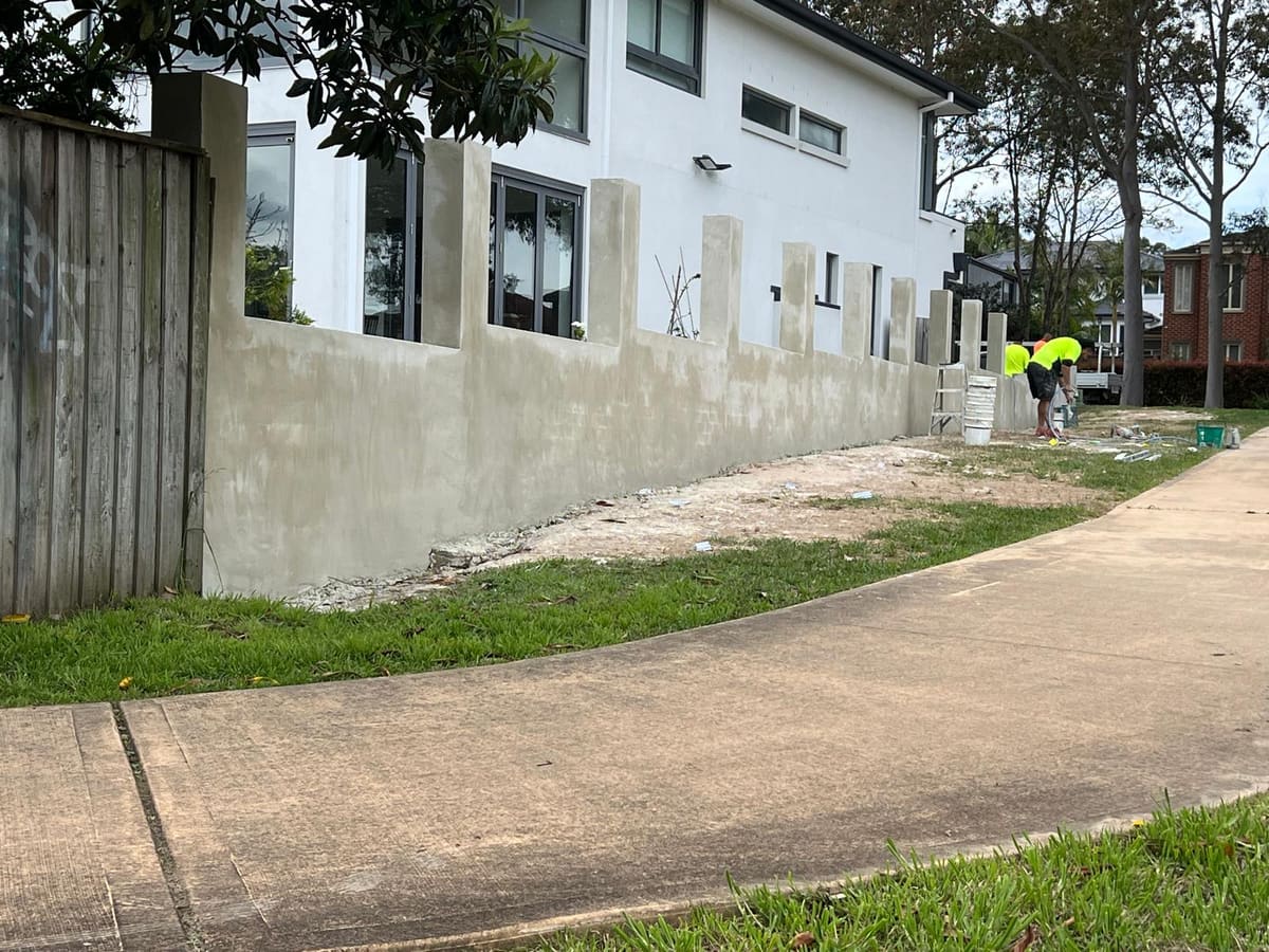 Long rendered front fence with evenly spaced piers being finished by a renderer outside a modern Sydney home