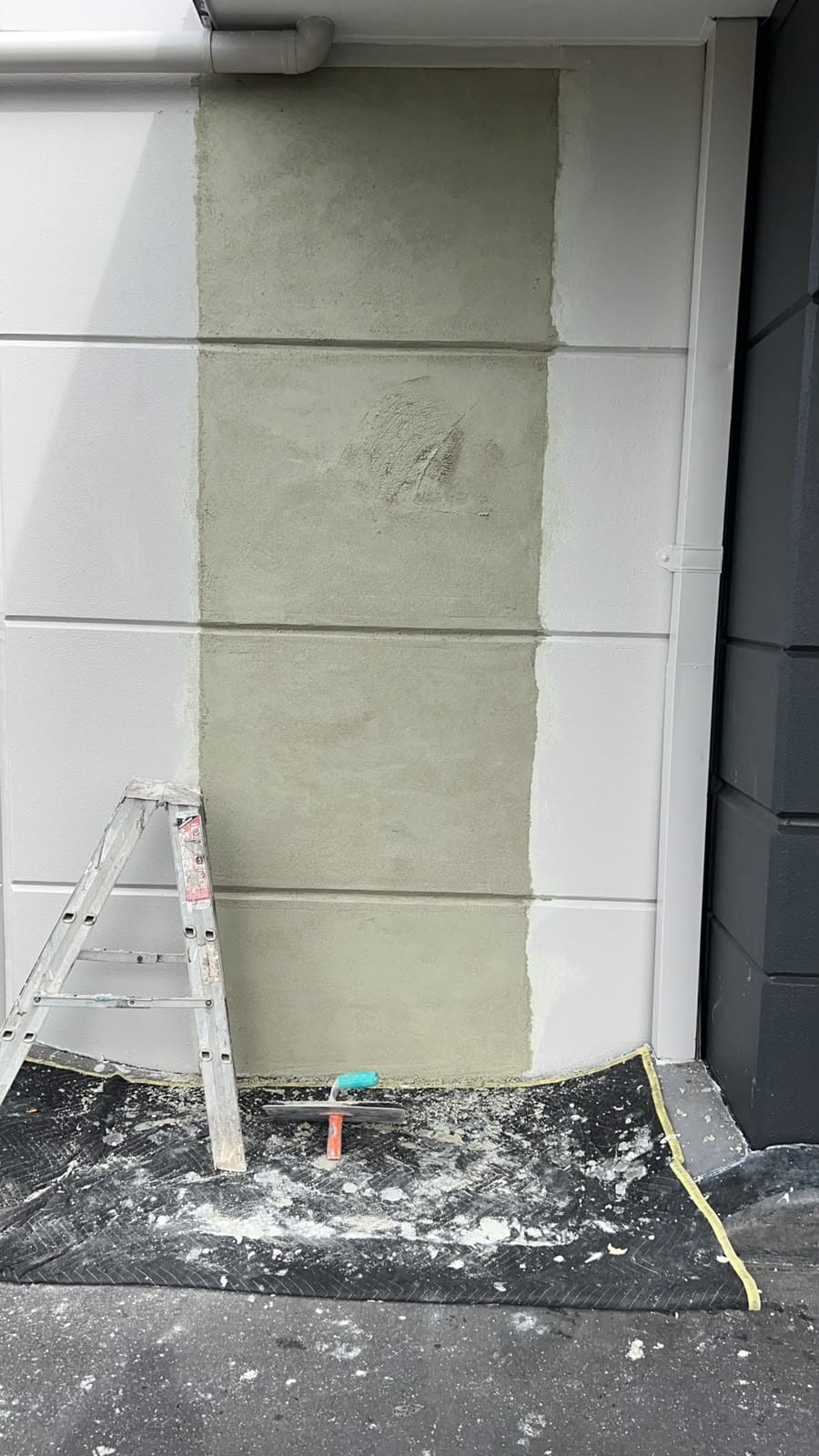 Fresh render patch blended into a panel wall beside a Sydney garage door with a trowel and ladder on the drop sheet