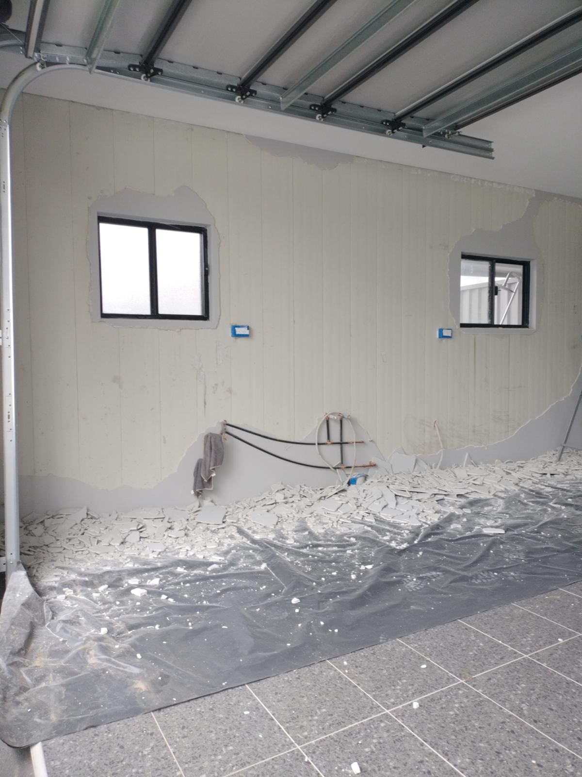 Failed render being stripped from a garage wall in Sydney with debris collected on plastic sheeting