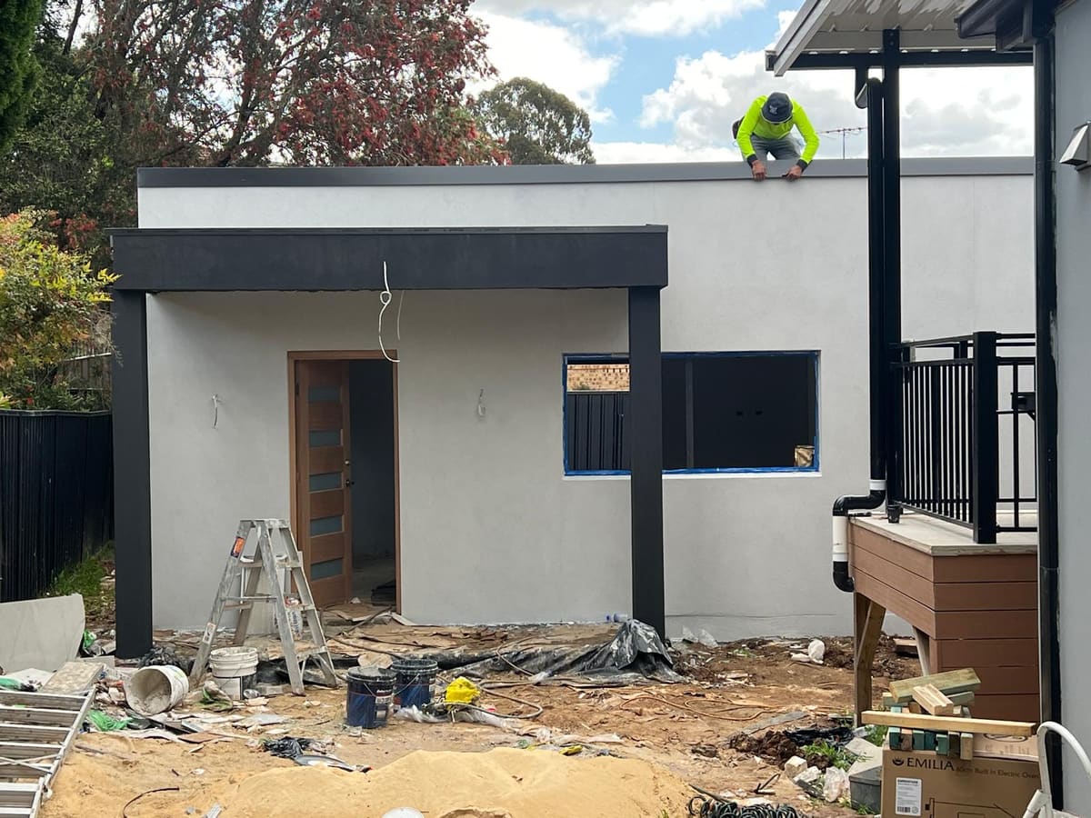 Newly rendered rear extension on a Sydney home with dark trim and a renderer working on the parapet