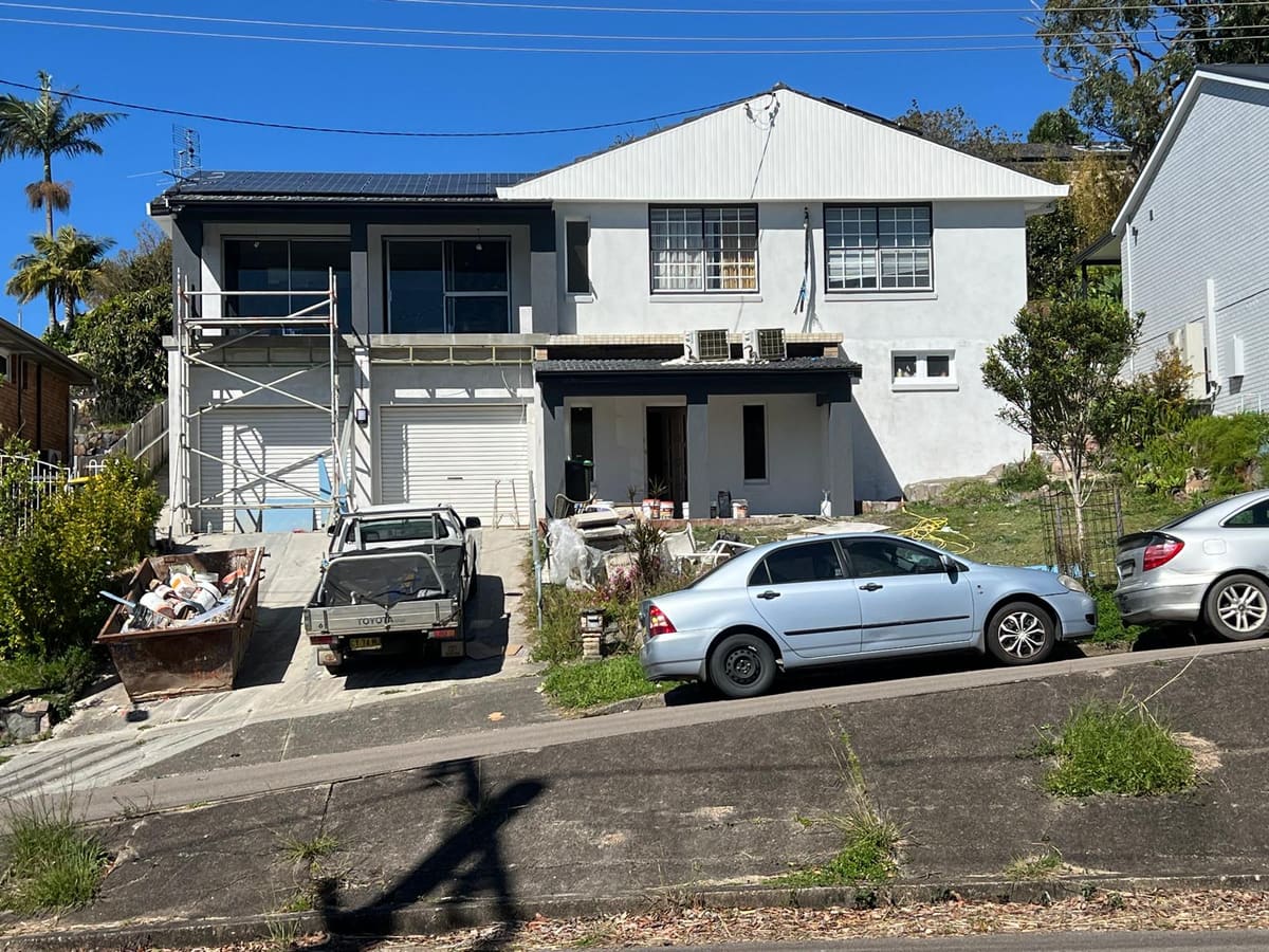 White rendered two storey house on a sloping Sydney street with scaffolding to the upper level