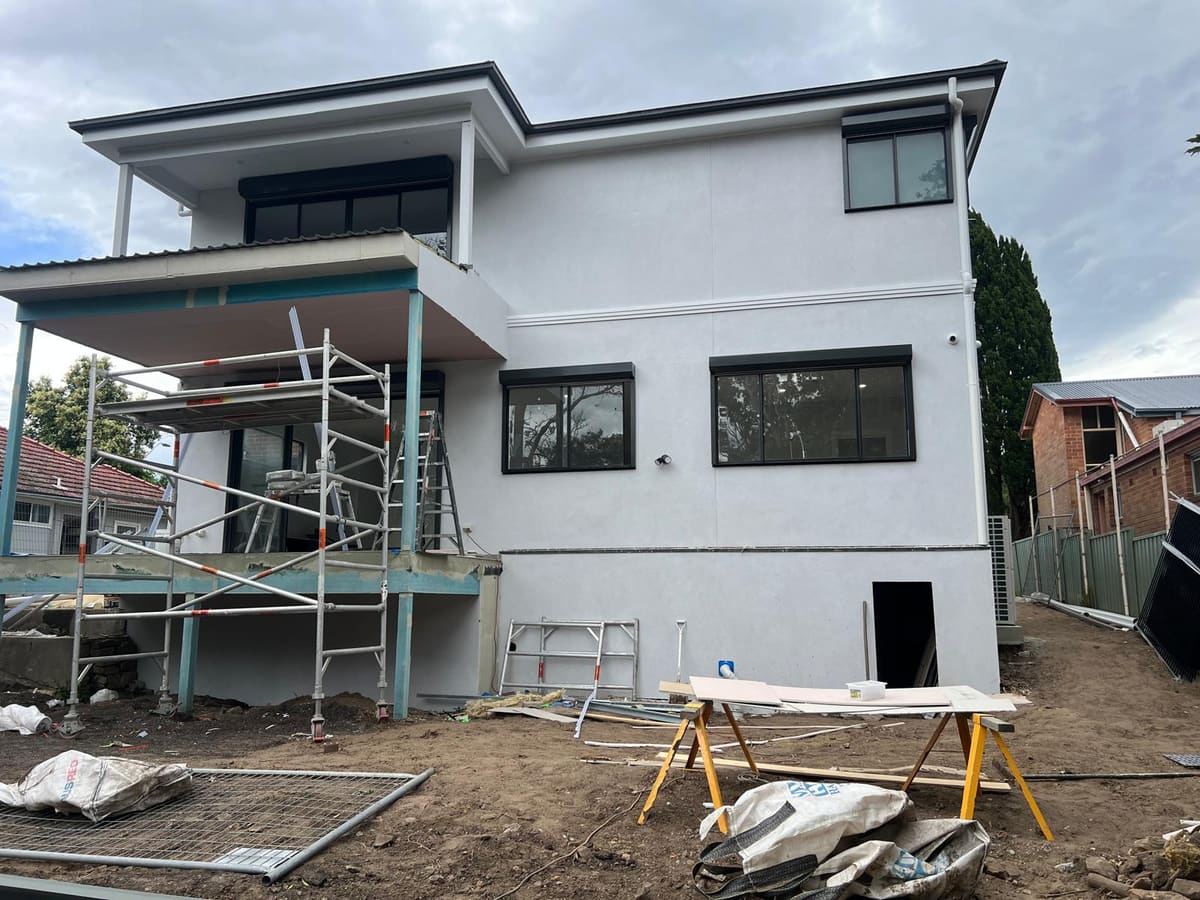 Rear of a large two storey Sydney house rendered in white with scaffolding still in place