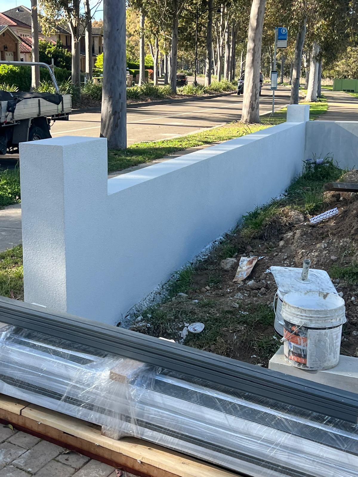 White rendered retaining wall running along a tree lined street in Sydney